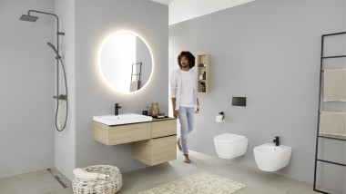 Een man loopt de badkamer in met een wastafel, wc, bidet en badkamermeubels uit de Geberit iCon-serie. Een man loopt de badkamer in met een wastafel, wc, bidet en badkamermeubels uit de Geberit iCon-serie.