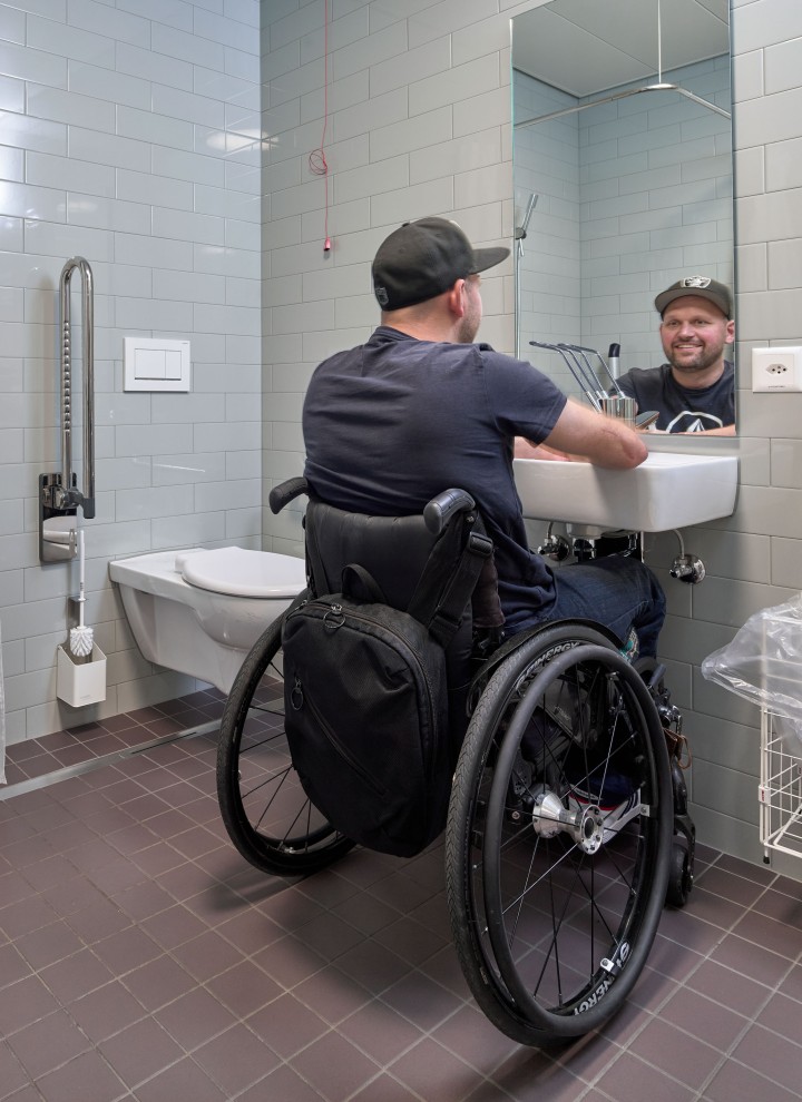 Peter Roos in een rolstoel bij de wastafel in een barrièrevrije badkamer (© Ben Huggler)