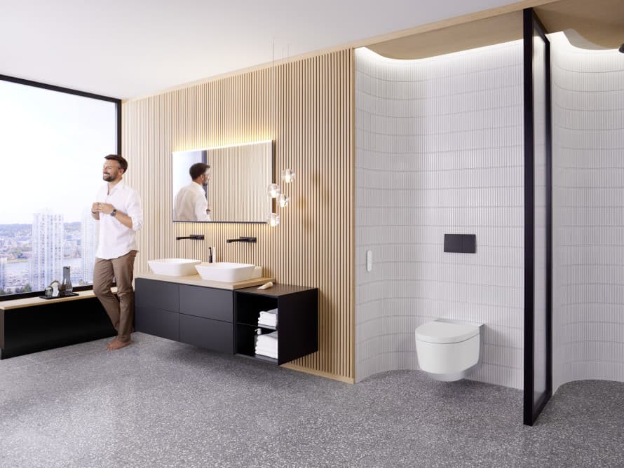 Man in een ruime badkamer met donkere meubels en een Geberit AquaClean douchewc Man in een ruime badkamer met donkere meubels en een Geberit AquaClean douchewc